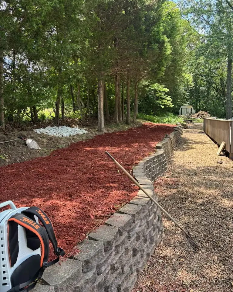 A long block retaining wall with a freshly mulched bed behind it running along a line of pines