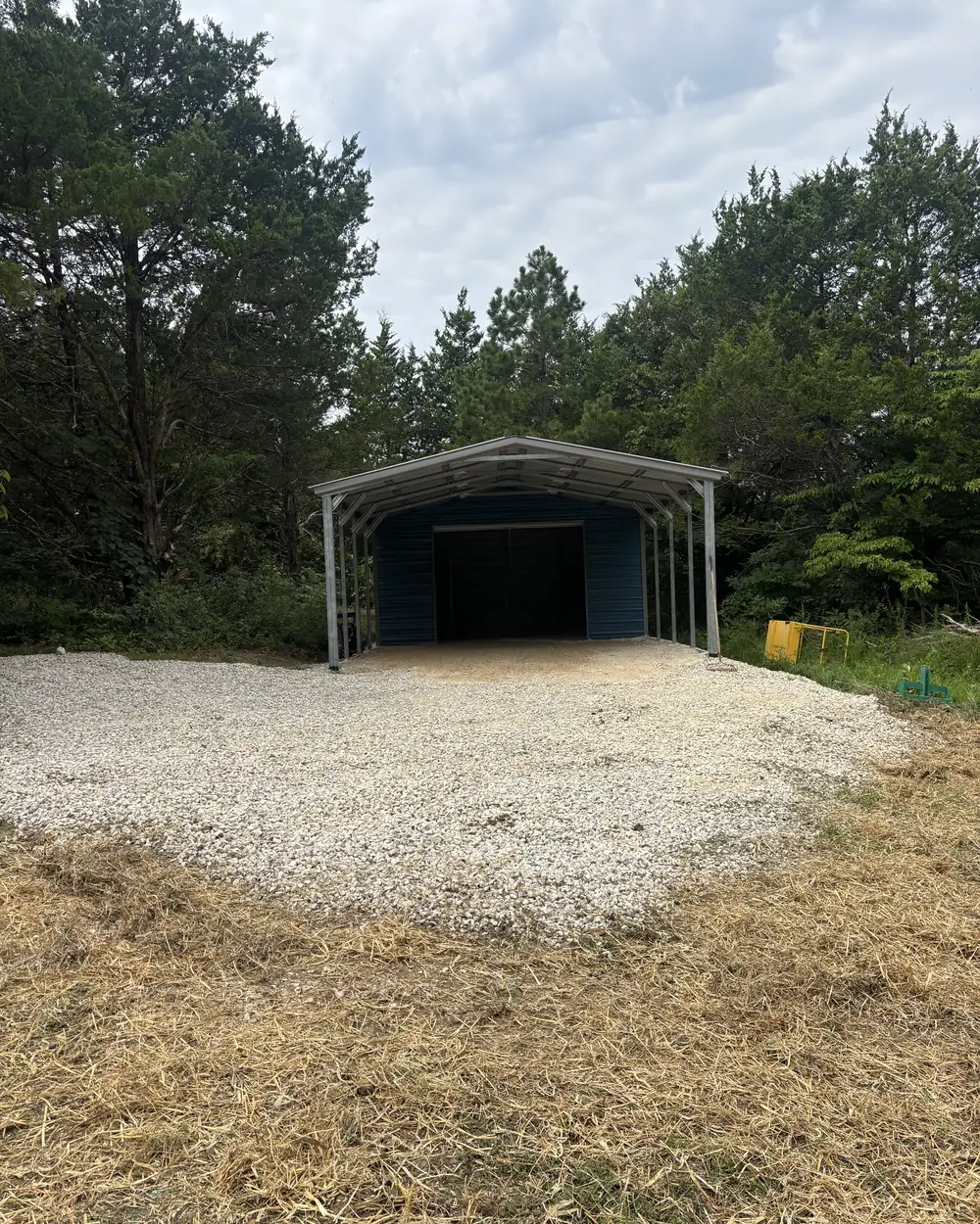 A compacted gravel pad built under a new steel carport, the ground around it cut to grade and strawed