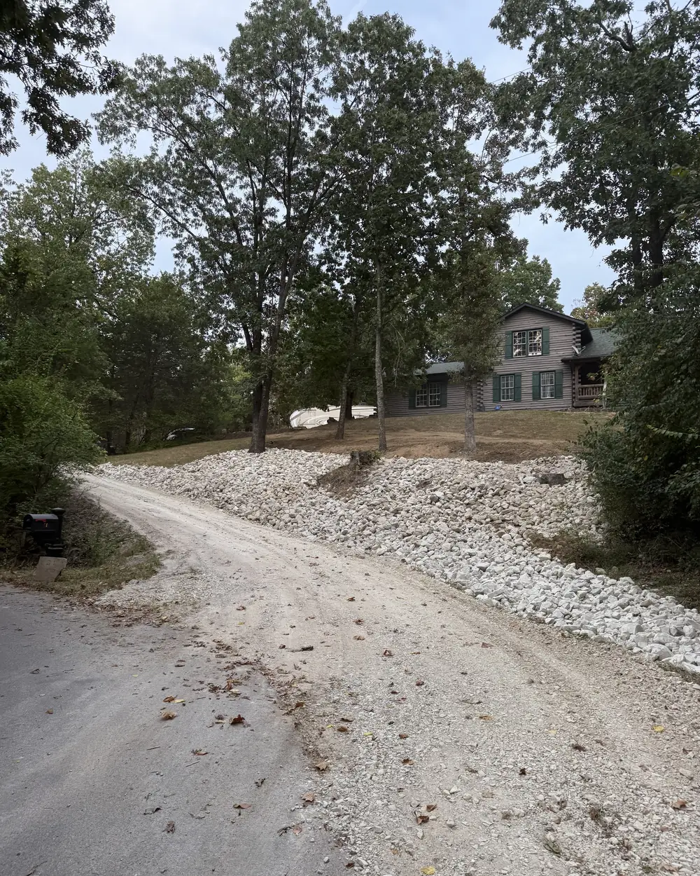 A bank of white rip-rap built up along the edge of a gravel driveway below a house, holding the slope off the track