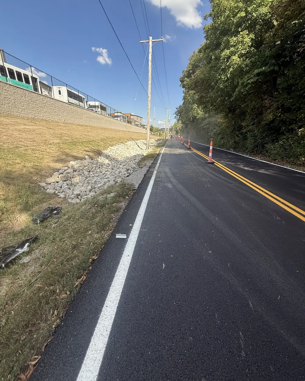 A finished rock-lined drainage channel along a rural road shoulder, white rip-rap set against a graded bank with traffic cones still out